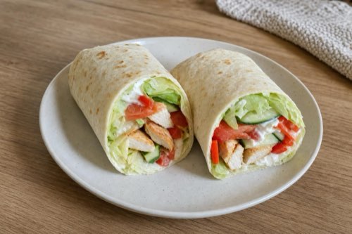 Kurací wrap s jogurtovým dresingom a zeleninou prekrojený na polovice na tanieri